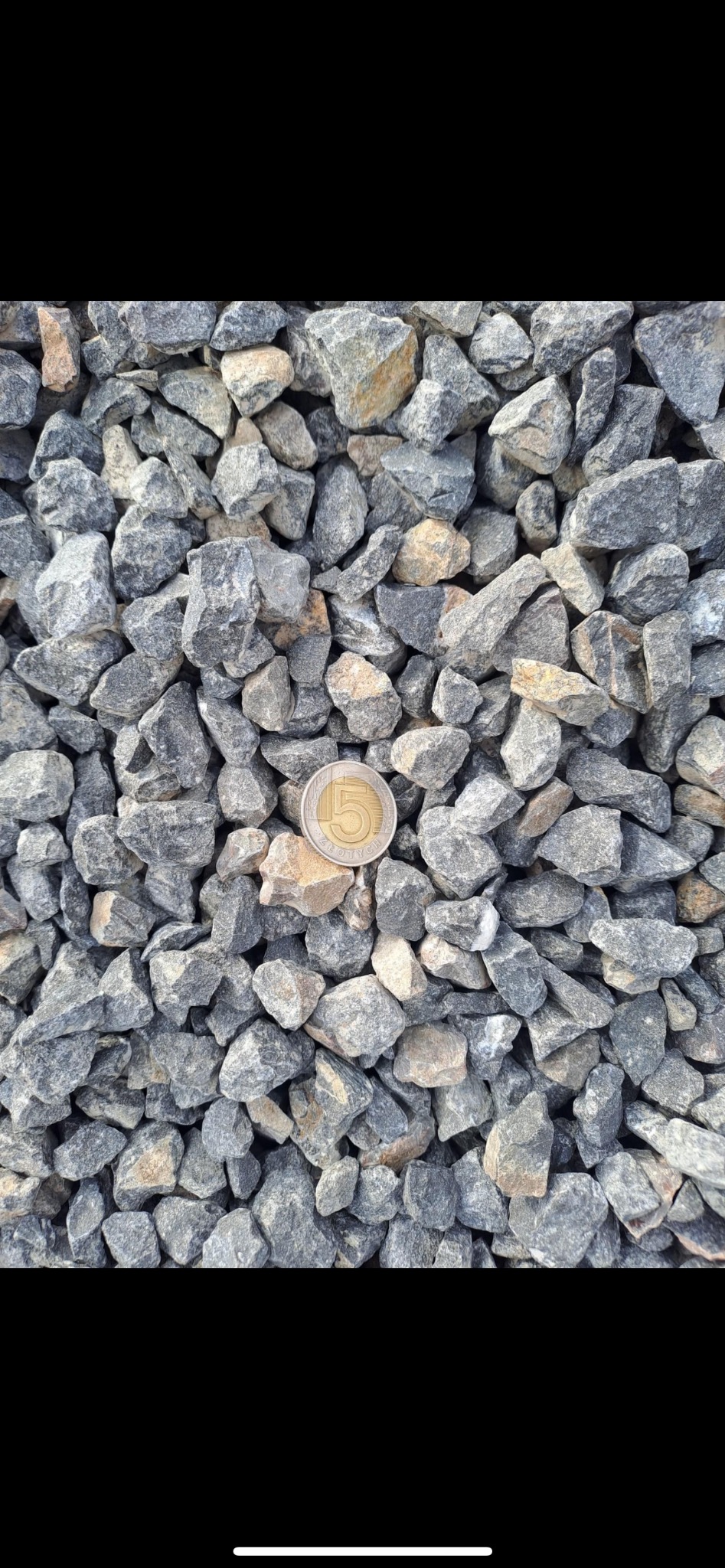 Szary tłuczeń granitowy o frakcji drobnej, z monetą 5 zł dla skali, oświetlony naturalnym światłem.