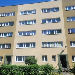 WASH WASH PIOTR REPLIN - Wielopiętrowy budynek mieszkalny z elewacją w odcieniach beżu i oliwki, widoczny z poziomu ulicy w słoneczny dzień.