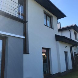 WASH WASH PIOTR REPLIN - Nowoczesny dom jednorodzinny z jasną elewacją i ciemną stolarką okienną, widoczny klimatyzator na ścianie, balkon z metalową balustradą.