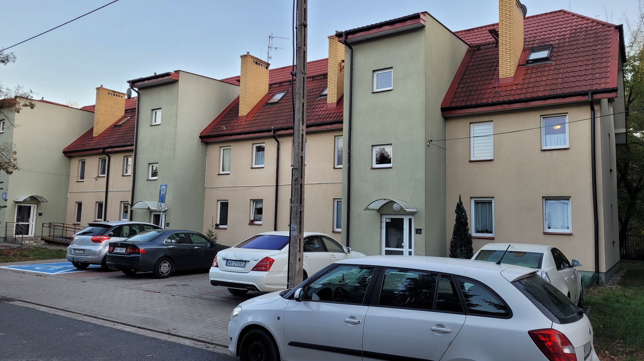 Wielorodzinny budynek po renowacji elewacji i dachu, z zaparkowanymi samochodami na pierwszym planie.