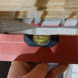 Grzegorz Bitner - Poziomica laserowa wskazuje poziom na drewnianej konstrukcji sufitu podwieszanego, widoczne profile montażowe.