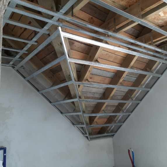 Metalowa konstrukcja sufitu podwieszanego z widoczną drewnianą konstrukcją stropu, przed montażem płyt gipsowo-kartonowych.