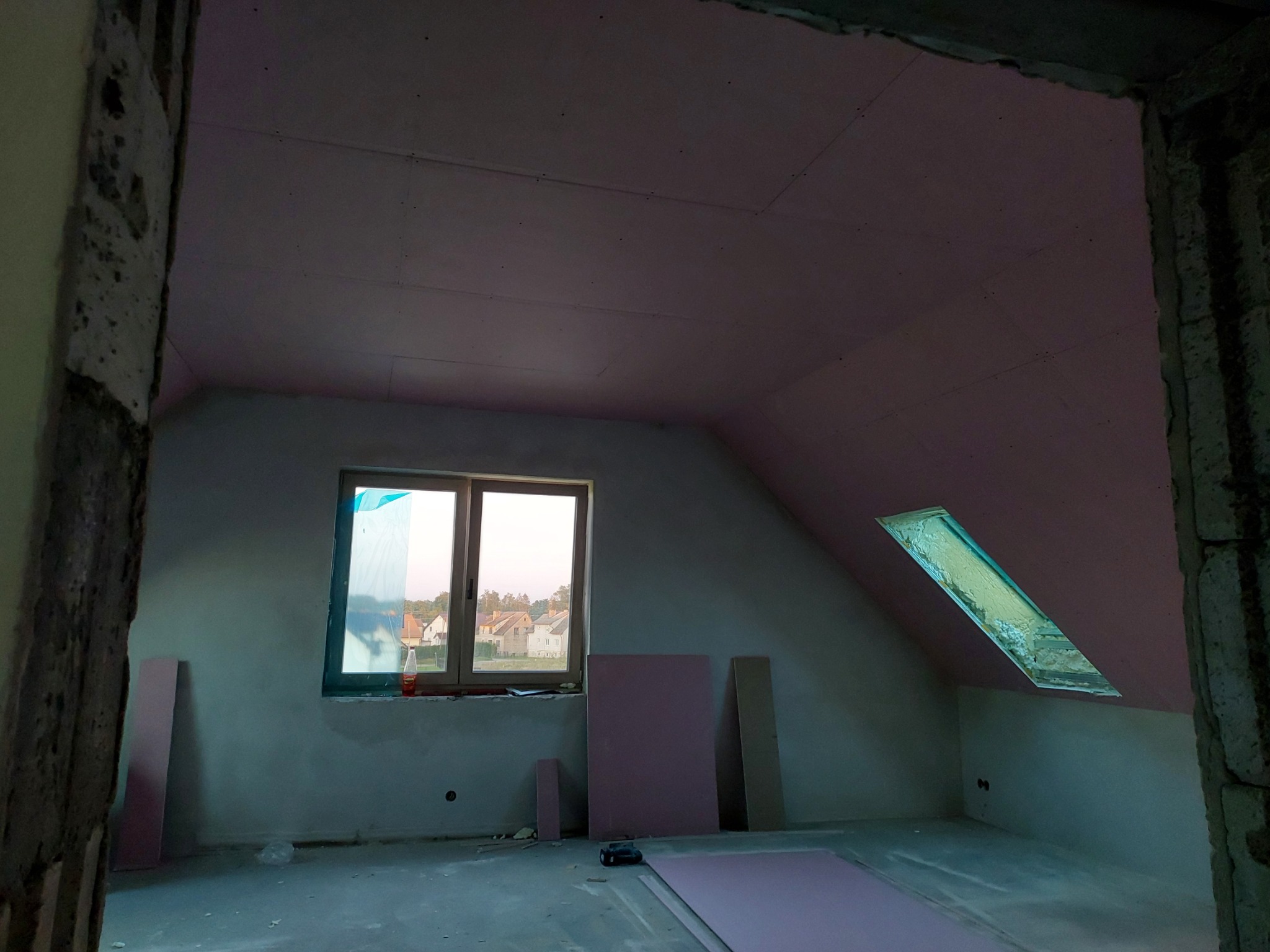 Poddasze w Kołczygłowach po montażu płyt karton gips, widoczne płyty różowe, okno dachowe i okno w ścianie szczytowej, surowe ściany.