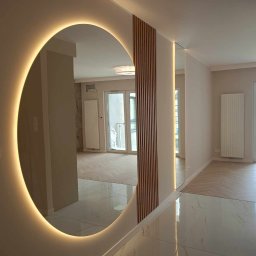 VIK-BUD VIKTOR SYDORCHUK - Nowoczesne wnętrze z okrągłym lustrem podświetlanym LED, drewnianymi lamelami na ścianie, błyszczącą podłogą z białego marmuru i parkietem w jodełkę w tle.