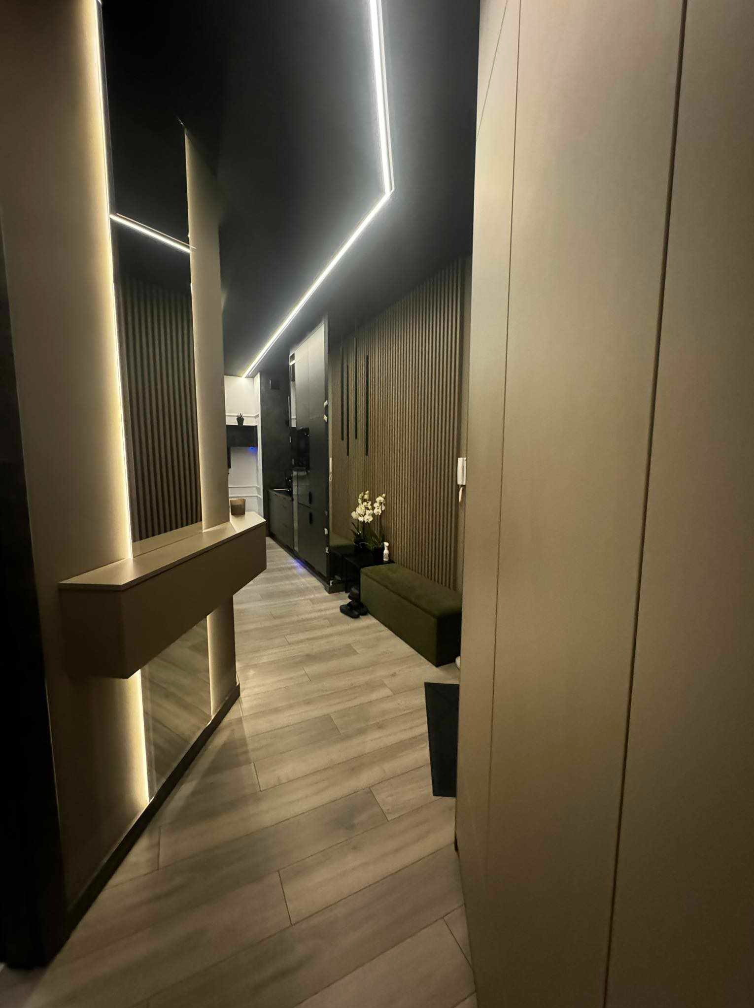 Nowoczesny przedpokój z podświetlanym lustrem, panelami ściennymi i drewnopodobną podłogą, oświetlenie LED w suficie.