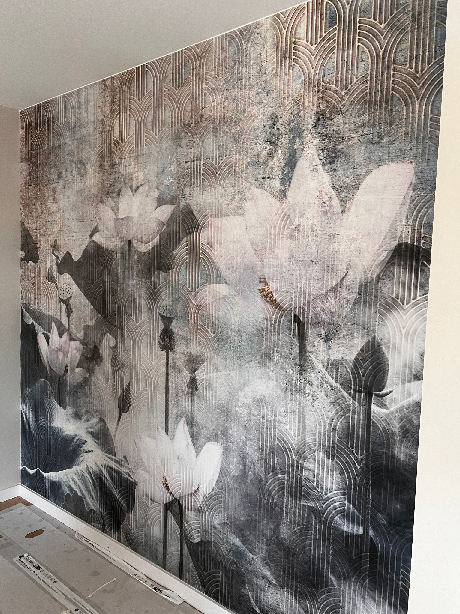 Ściana po tapetowaniu z motywem kwiatów lotosu i wzorem art deco, widoczne niedokończone prace przy podłodze.