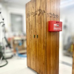 PAPAJ Sp. z o.o. - Drewniana szafa z motywem górskim i apteczką przymocowaną z boku, widoczna w warsztacie.