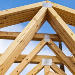 M.A.M. DREWNO MARCIN STACHOWIAK - Fragment drewnianej więźby dachowej z metalowymi łącznikami na tle błękitnego nieba. Widoczne detale konstrukcji i łączeń.