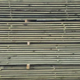 Stos desek o zielonkawym odcieniu, ułożonych równo jedna na drugiej i spiętych zielonymi taśmami. Widoczne przekładki między warstwami drewna.