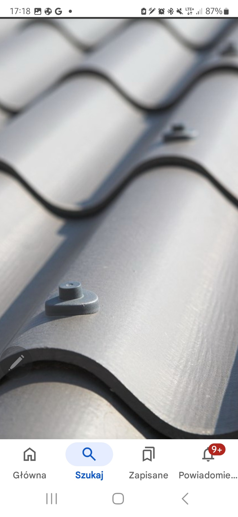 Szczegółowy widok na szare dachówki ceramiczne z widocznymi elementami mocującymi, ułożone w falisty wzór. Ujęcie z bliska, z ostrością na fakturę i detale.