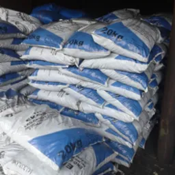 Stos worków 20kg z paliwem do kotłów, biało-niebieskie opakowania z napisem EKO-GROSZEK, widoczne w magazynie, oświetlenie magazynowe.