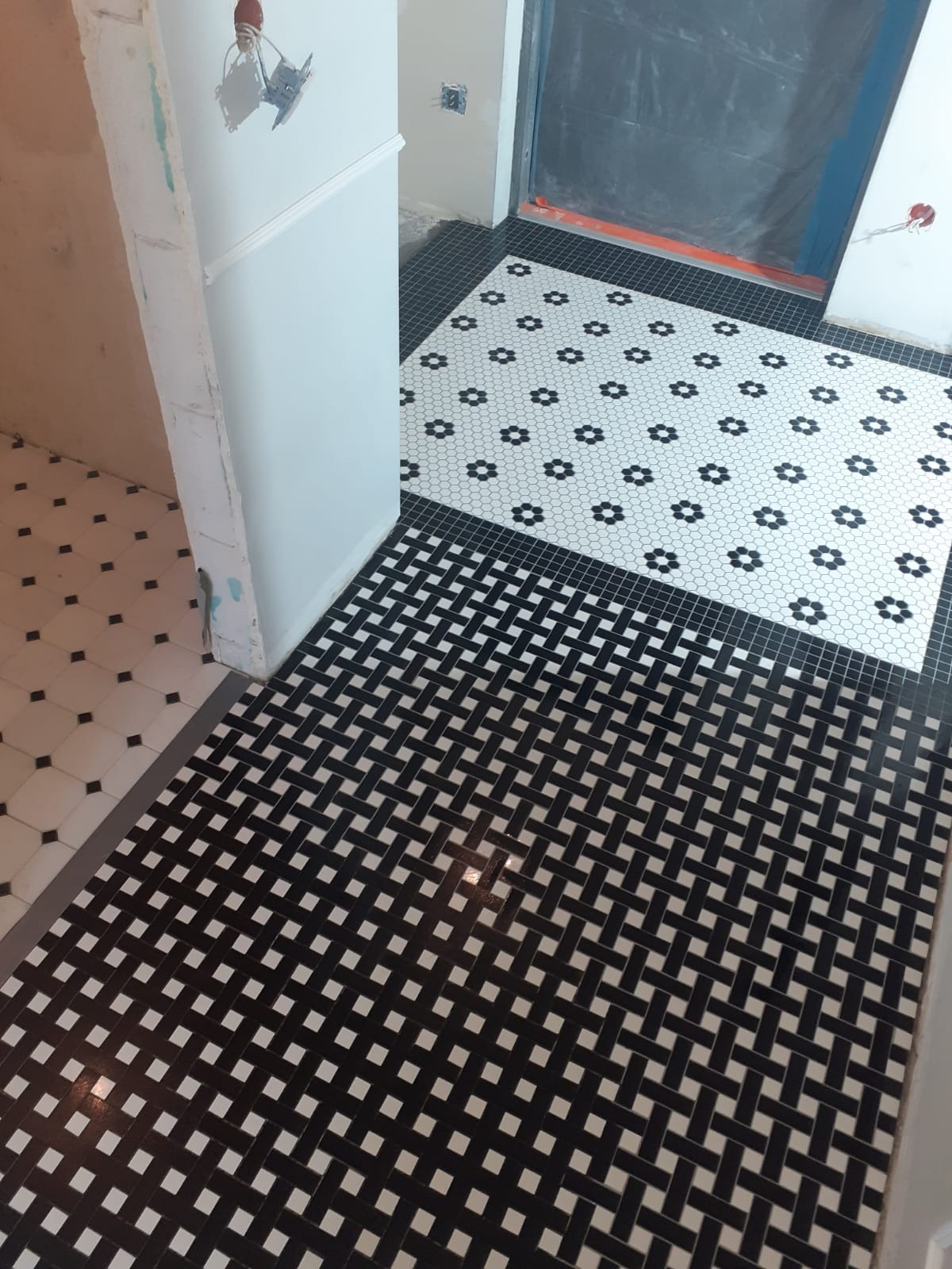 Podłoga wyłożona czarno-białą mozaiką w dwóch wzorach: jeden z motywem kwiatowym, drugi w kształcie plecionki, widoczne niedokończone ściany i instalacje.