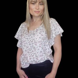 AW Designer Aleksandra Wisińska - Kobieta w kwiecistej bluzce z krótkim rękawem i czarnych spodniach na czarnym tle, z blond włosami i grzywką.