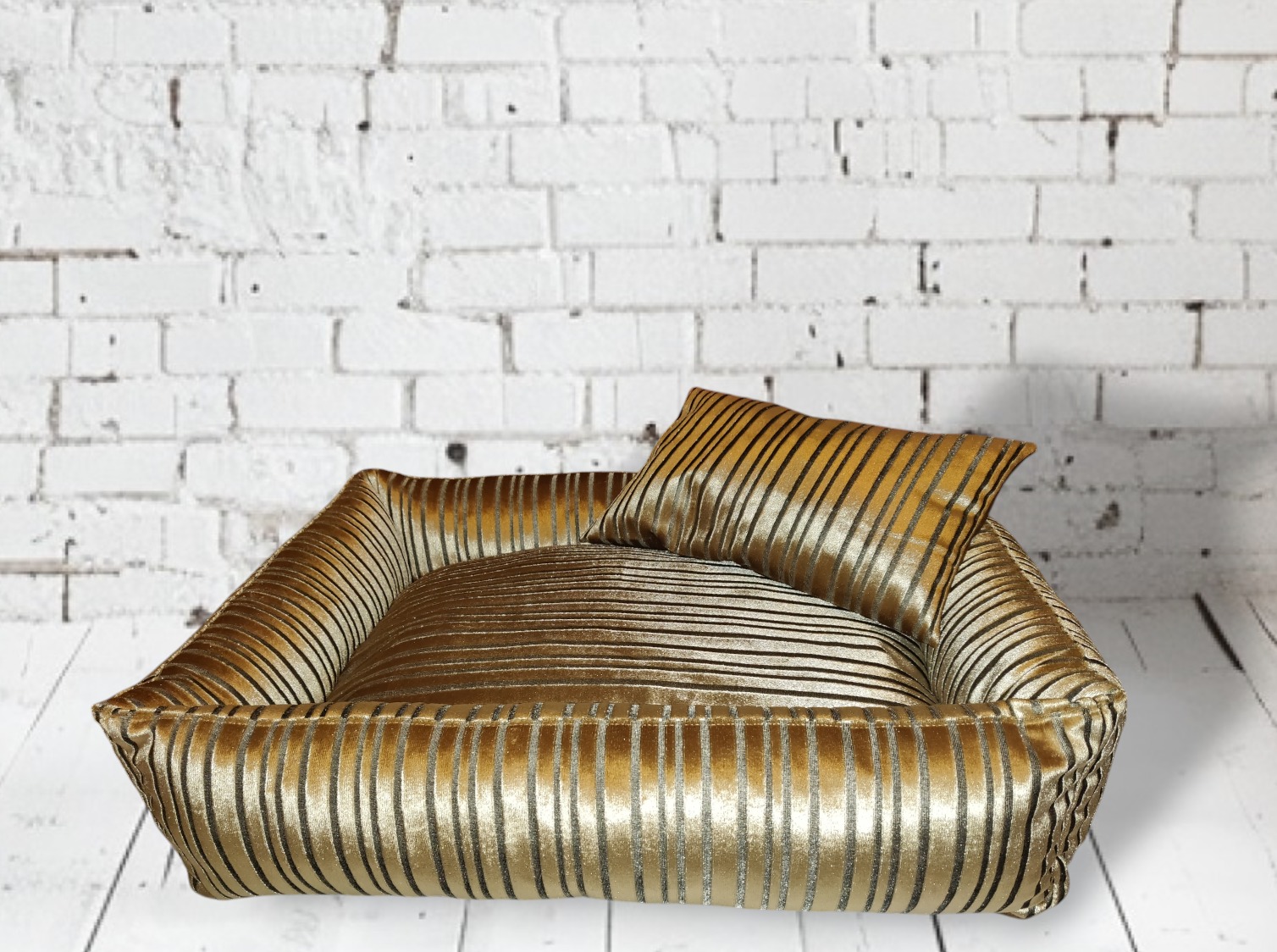 Eleganckie, złoto-czarne, prążkowane legowisko dla psa z poduszką na tle białej, ceglanej ściany.