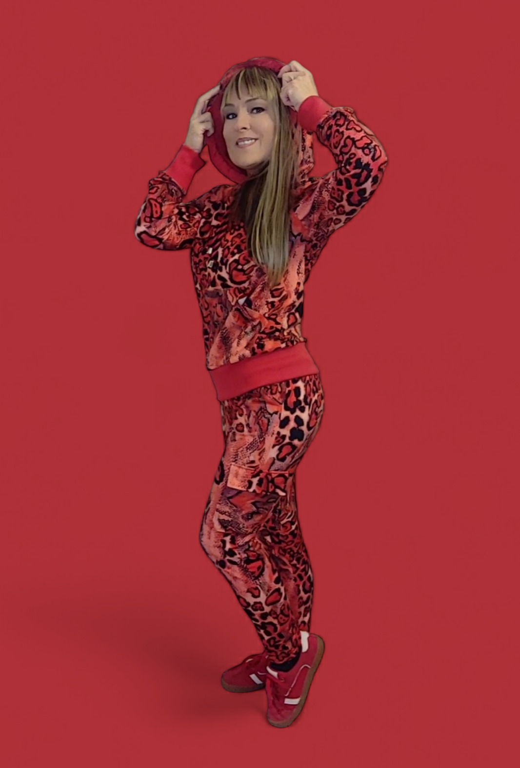 Kobieta w czerwonym dresie w panterkę z kapturem, pozuje na jednolitym czerwonym tle.