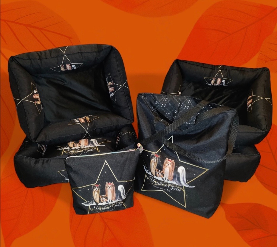 Zestaw czarnych akcesoriów dla psów z nadrukiem logo i rysunkiem psów rasy York: legowiska, torba i kosmetyczka, na pomarańczowym tle.