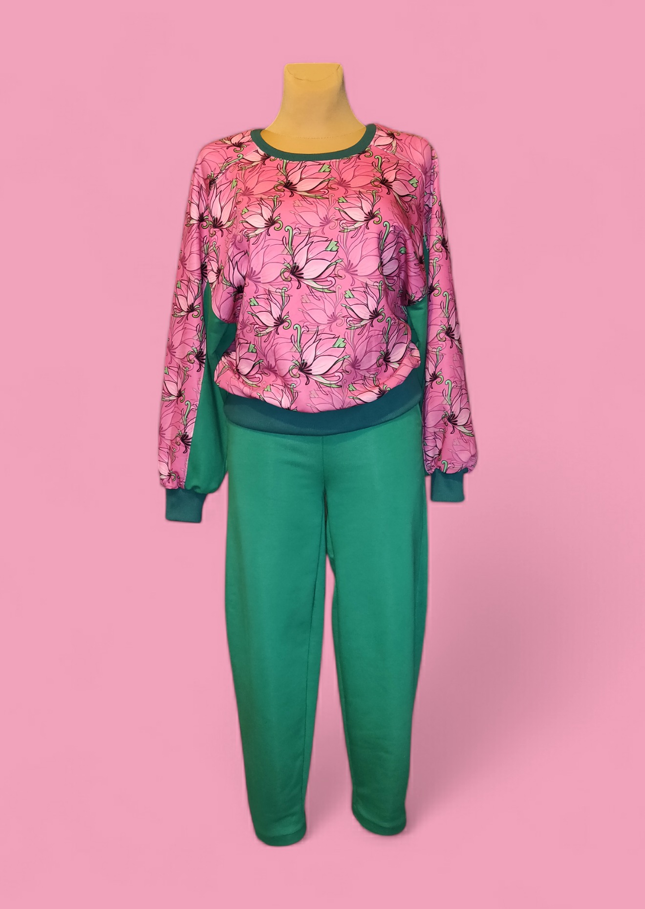 Damski dres: różowa bluza z długim rękawem w kwiaty lotosu i gładkie zielone spodnie, prezentowane na manekinie na tle różowego studia.