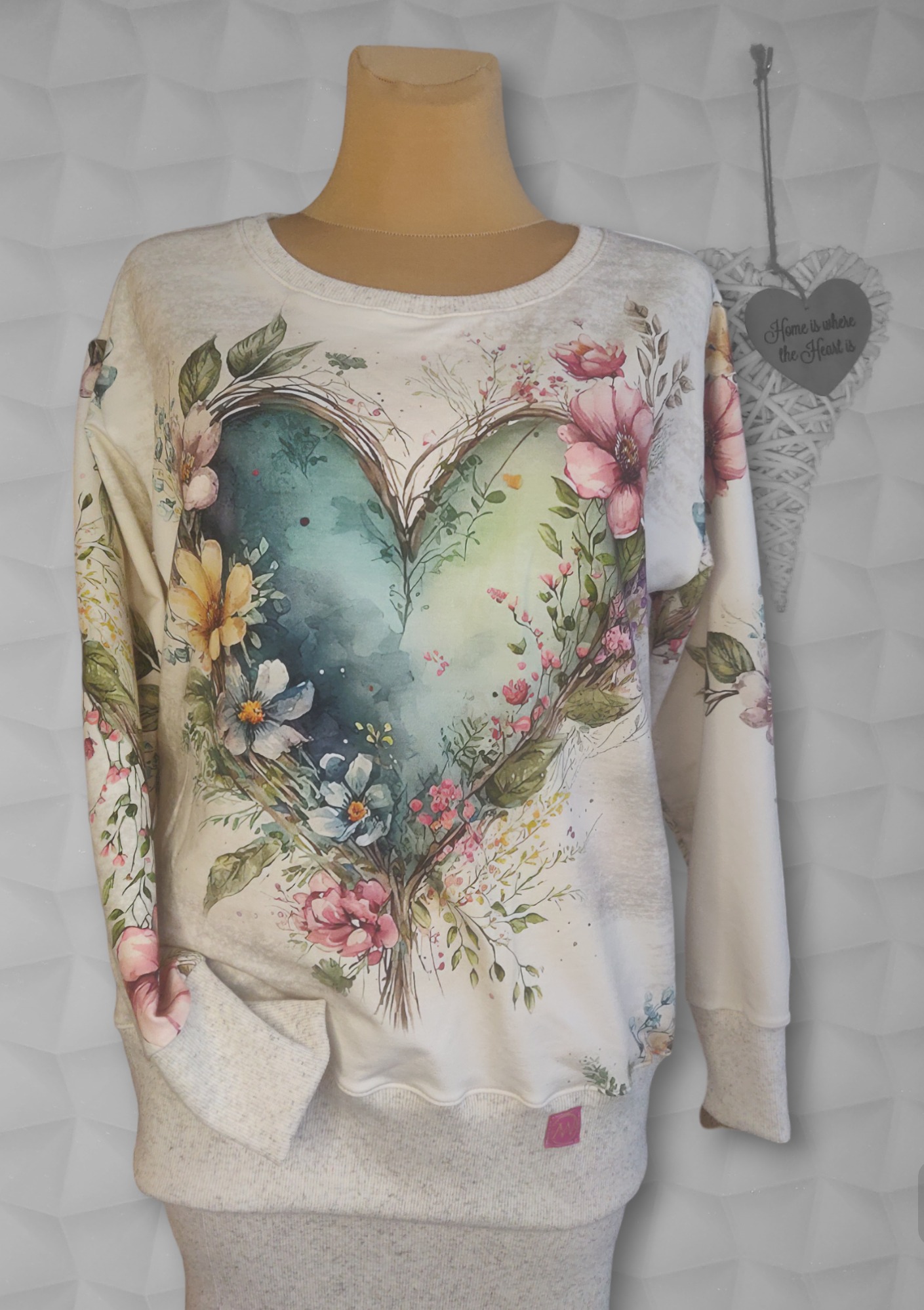 Bluza damska z nadrukiem akwarelowego serca oplecionego kwiatami, prezentowana na manekinie na tle białej, teksturowanej ściany.