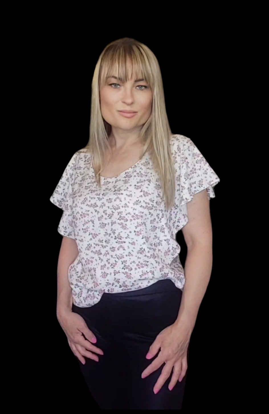 Kobieta w kwiecistej bluzce z krótkim rękawem i czarnych spodniach na czarnym tle, z blond włosami i grzywką.