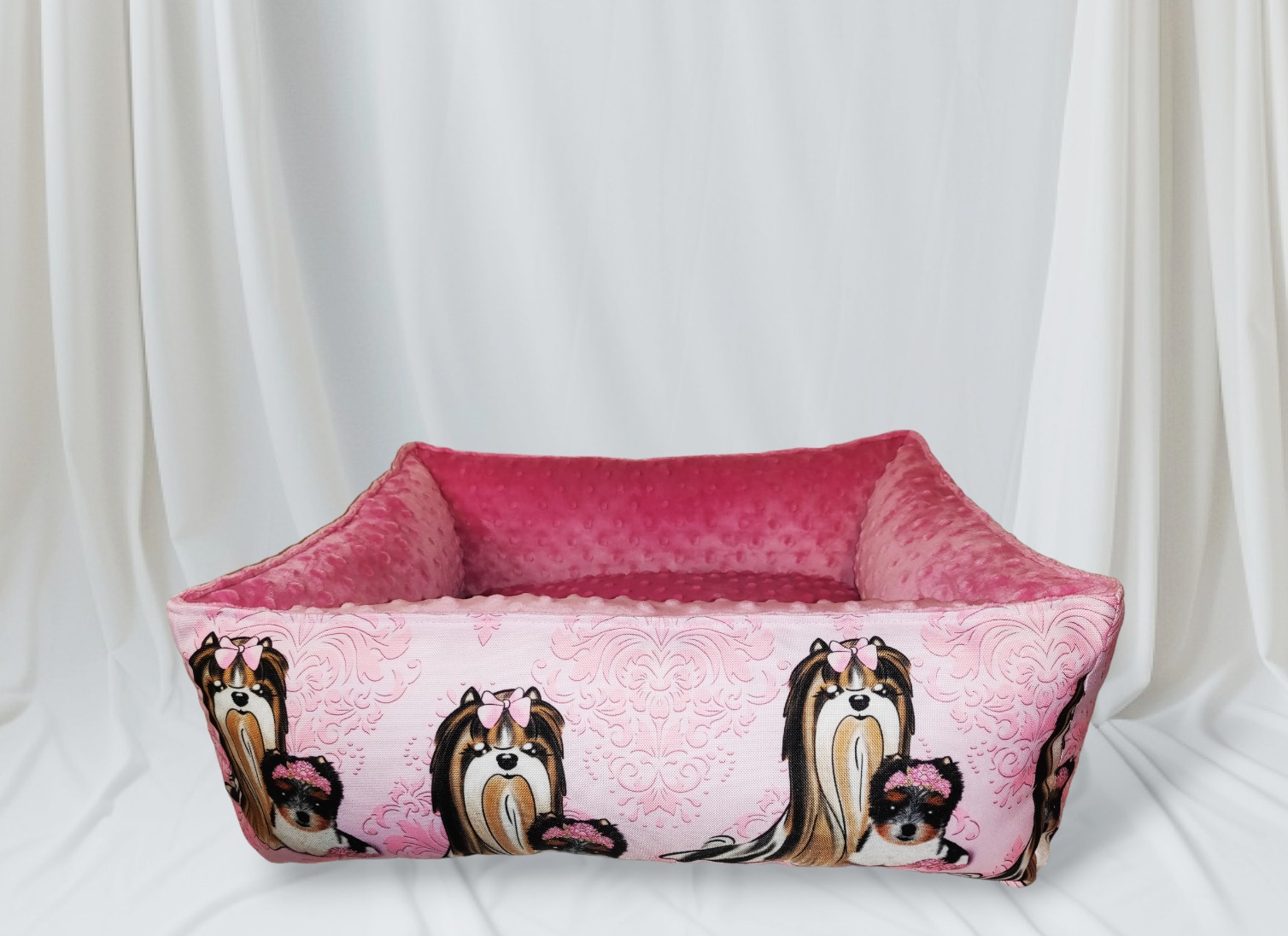 Różowe legowisko dla psa z wzorem przedstawiającym yorki na tle białych zasłon.