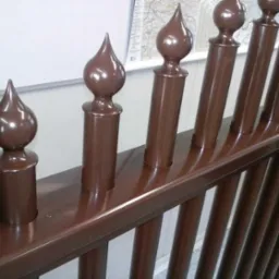 Błyszcząca, brązowa balustrada schodowa z dekoracyjnymi zakończeniami w kształcie łezki i kulki, widoczna z bliskiej perspektywy.