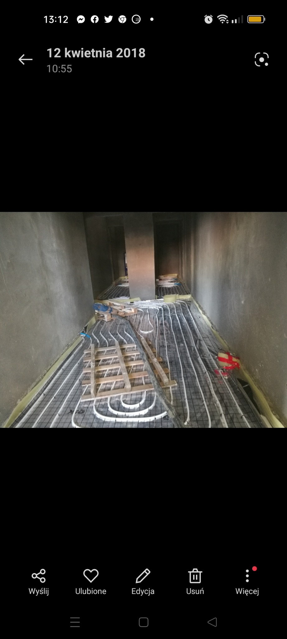 Montaż ogrzewania podłogowego w surowym wnętrzu, widoczne rury ułożone na siatce, drewniane podpory i ściany w stanie deweloperskim.