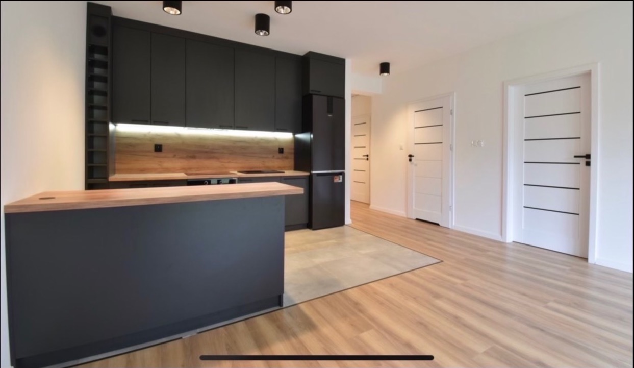 Nowoczesna kuchnia w odcieniach szarości i drewna, z wyspą kuchenną i dwiema białymi drzwiami z czarnymi akcentami w tle.