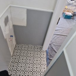 P.S. Majster Expert - Wnętrze łazienki w trakcie remontu, widoczne świeżo ułożone czarno-białe płytki podłogowe o wzorze geometrycznym, szare ściany z białymi listwami, przygotowane do dalszych prac wykończeniowych,...