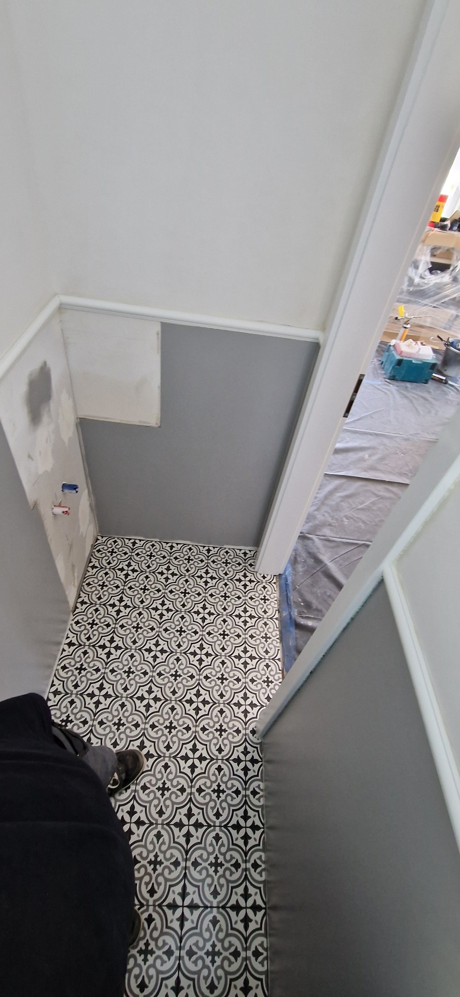 Wnętrze łazienki w trakcie remontu, widoczne świeżo ułożone czarno-białe płytki podłogowe o wzorze geometrycznym, szare ściany z białymi listwami, przygotowane do dalszych prac wykończeniowych,...