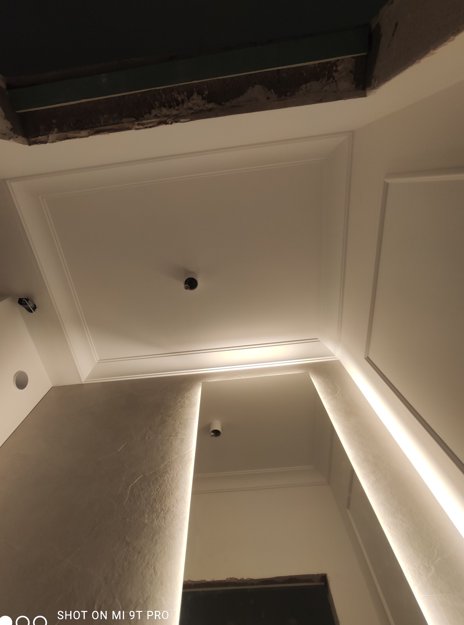 Fragment sufitu z dekoracyjną sztukaterią i przygotowanym otworem na oświetlenie, widoczne niedokończone prace wykończeniowe w górnej części kadru.