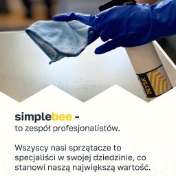 Simplebee Khrystyna Kuzmenko - Osoba w niebieskich rękawicach czyści powierzchnię płaską szarą ściereczką z mikrofibry, obok stoi biała butelka ze spryskiwaczem i etykietą 'Błysk', widoczne drobne krople wody.
