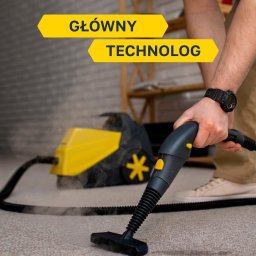 Simplebee Khrystyna Kuzmenko - Czyszczenie dywanu parownicą: dłoń w zegarku prowadzi dyszę po jasnym dywanie, z tyłu żółto-czarny odkurzacz parowy. Para unosi się podczas pracy.