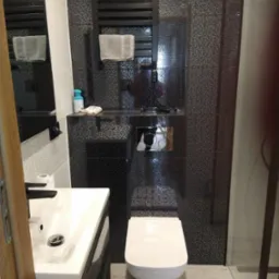 Nowoczesna łazienka z czarno-białą mozaiką na ścianach, wiszącą toaletą, umywalką z czarną szafką i grzejnikiem drabinkowym z ręcznikiem.