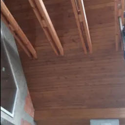 Drewniana podbitka dachowa z widocznymi elementami konstrukcyjnymi, betonowy filar i fragment ściany budynku z oknem.