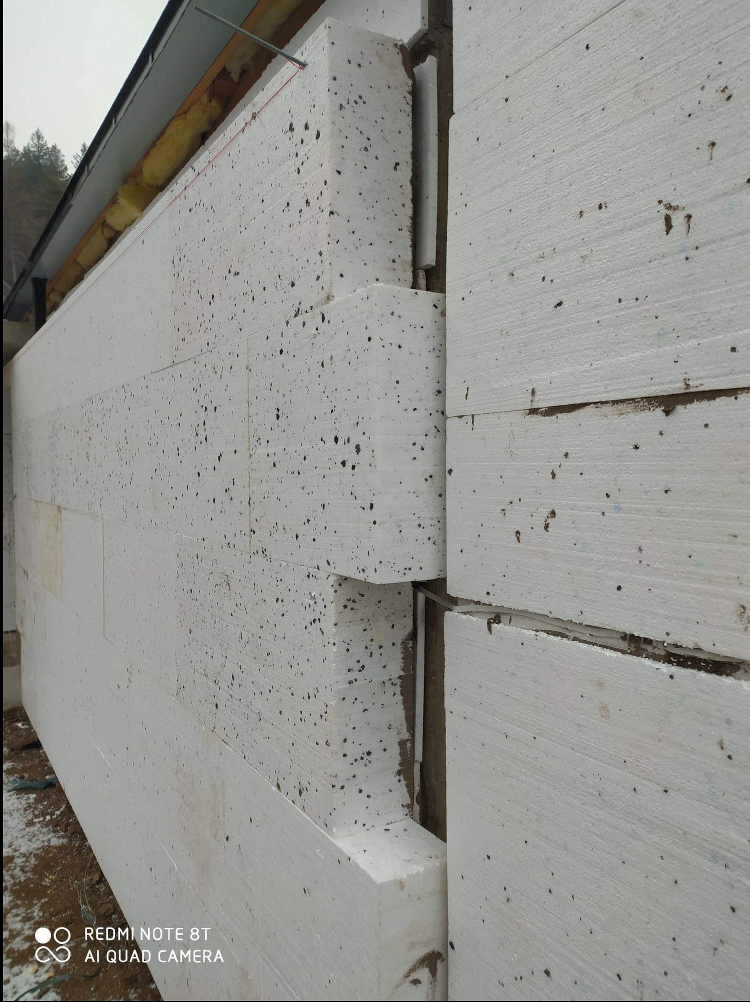 Ocieplenie ściany zewnętrznej budynku płytami styropianowymi z widoczną warstwą izolacji stropu.