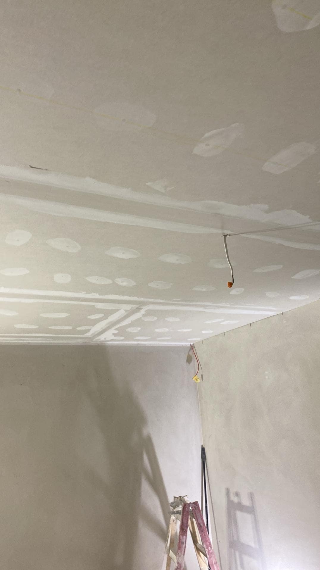 Wnętrze w trakcie prac wykończeniowych: sufit z płyt gipsowo-kartonowych, widoczne łączenia i szpachlowane miejsca po wkrętach, wystające przewody elektryczne, drabina malarska w rogu pomieszczenia.