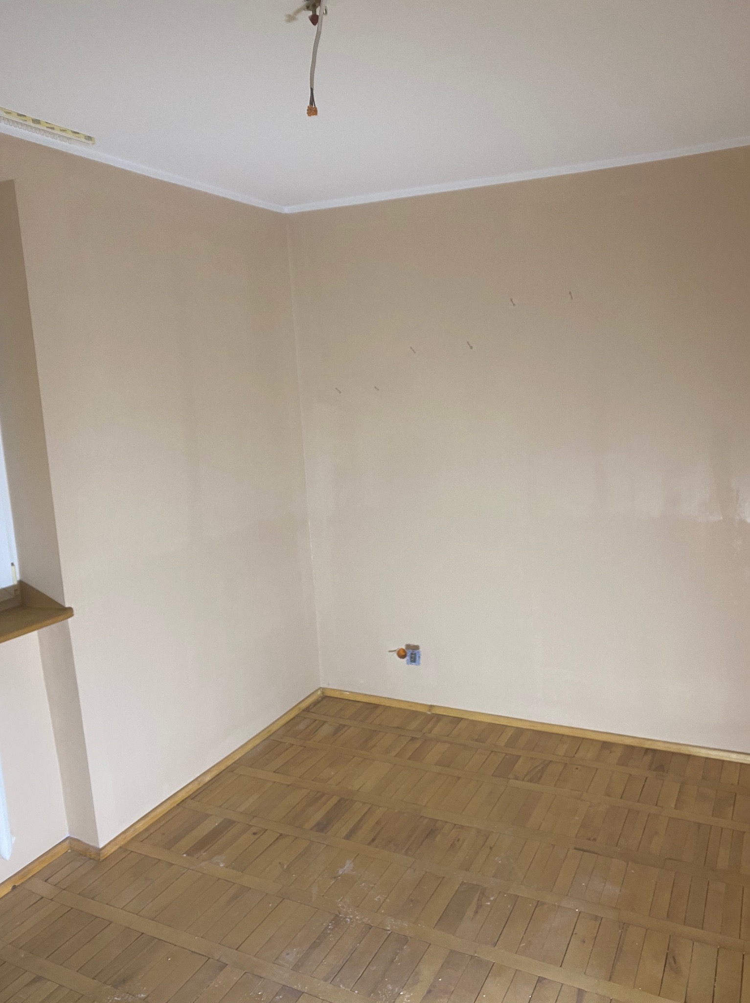 Pusty pokój po nałożeniu gładzi, z widocznymi śladami po szpachlowaniu na ścianach i drewnianą podłogą w jodełkę, przygotowany do dalszych prac wykończeniowych.