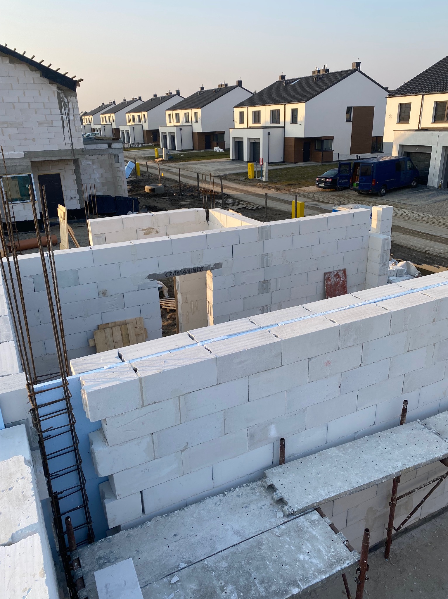 Wznoszenie ścian z białych bloczków betonu komórkowego na budowie osiedla domów jednorodzinnych, widoczne zbrojenia pionowe i podesty rusztowań.