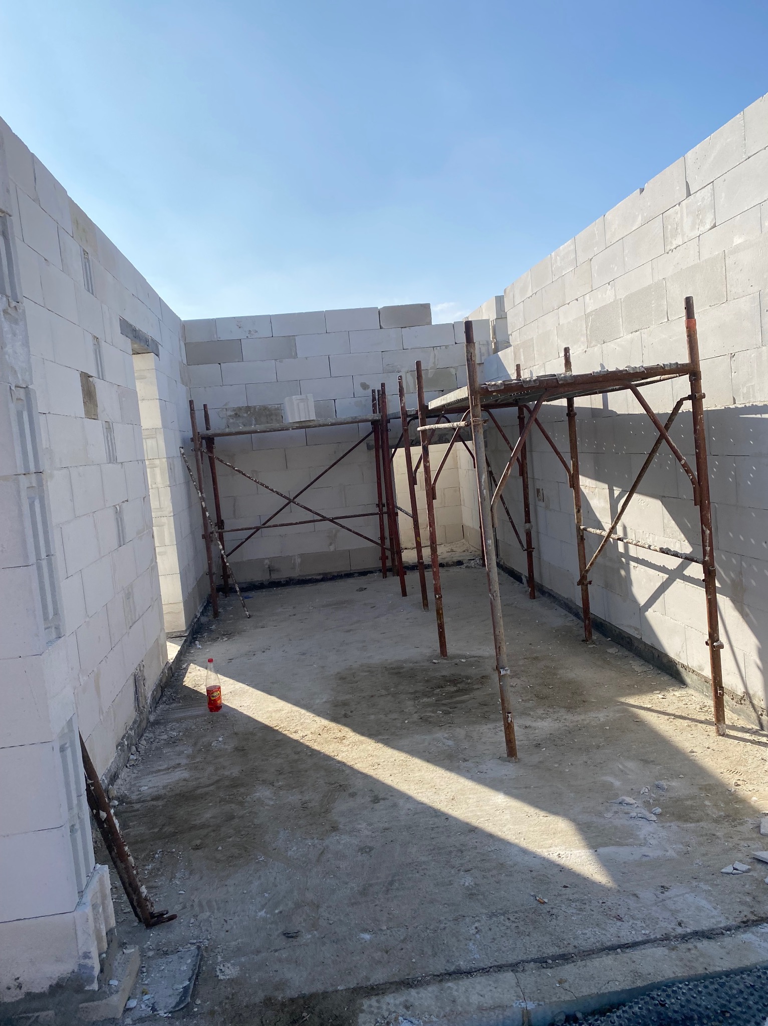 Wnętrze w trakcie budowy z białych bloczków, widoczne rusztowanie i butelka z napojem na podłodze.