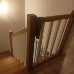 Widok z góry na drewniane schody z białymi balustradami, oświetlone ciepłym światłem, z elementem garderoby zawieszonym na poręczy.