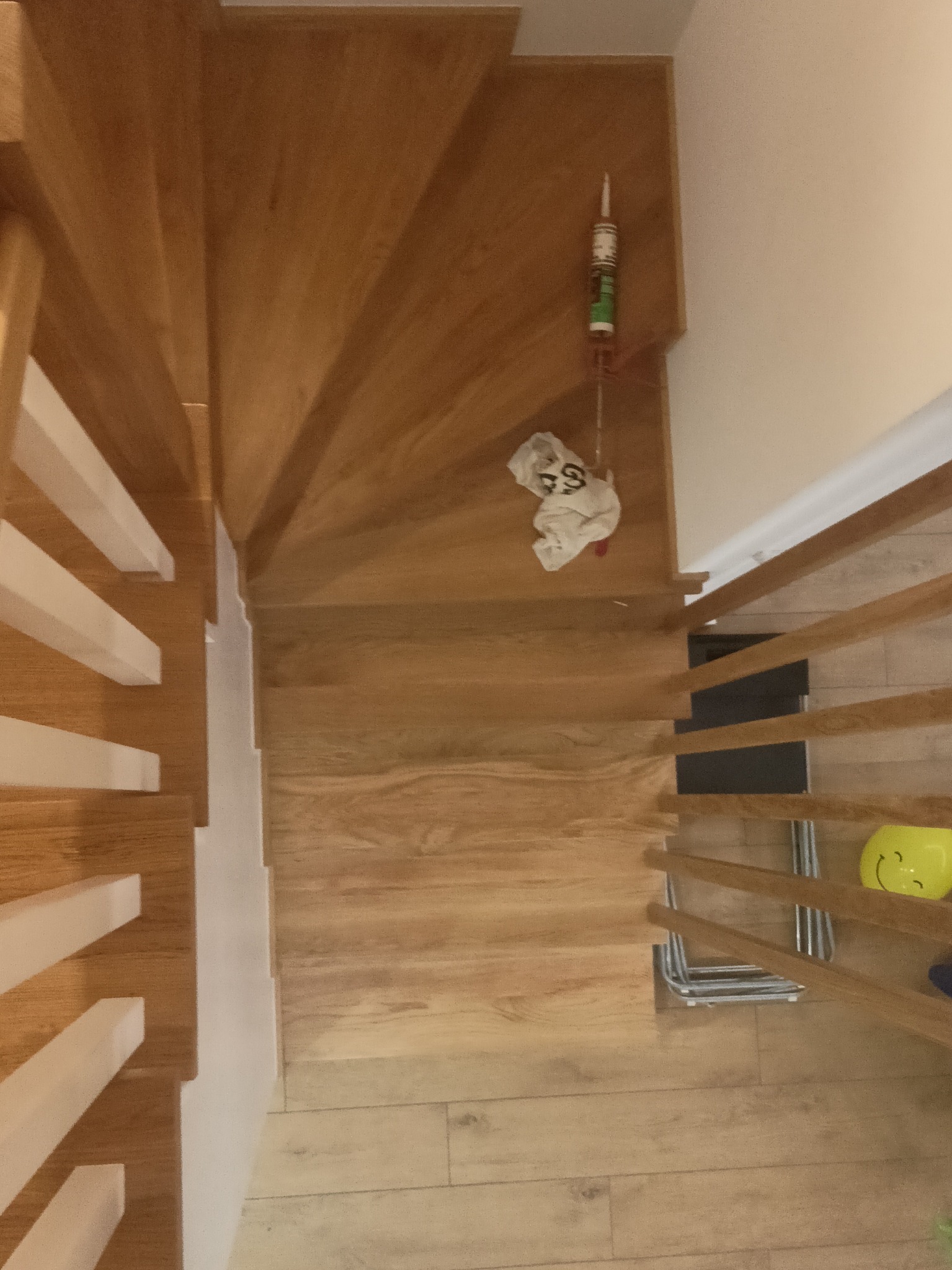 Widok z góry na drewniane schody z białymi balustradami, z widocznymi narzędziami i akcesoriami montażowymi na podeście.