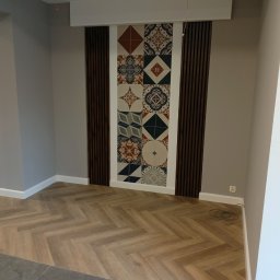 Majster Art Jakub Baran - Salon po remoncie: ułożona podłoga z paneli w jodełkę, ściana z dekoracyjnymi płytkami w stylu patchwork, obramowana drewnianymi lamelami.