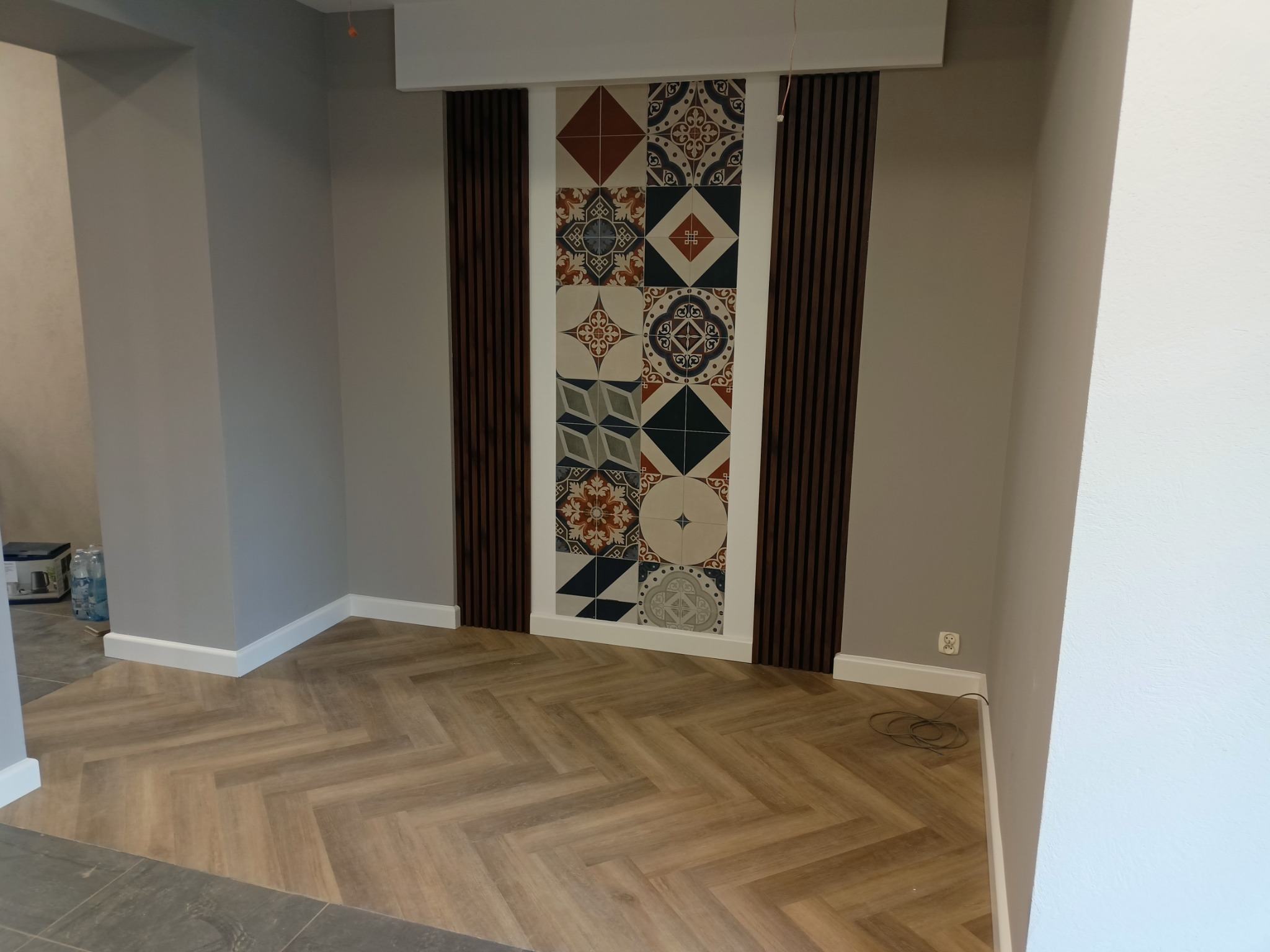 Salon po remoncie: ułożona podłoga z paneli w jodełkę, ściana z dekoracyjnymi płytkami w stylu patchwork, obramowana drewnianymi lamelami.