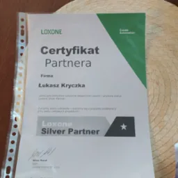 Certyfikat partnerstwa Loxone Silver Partner dla firmy Łukasz Kryczka, leżący na plecionej podkładce, z widocznym podpisem CEO Loxone Poland.