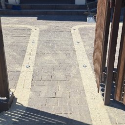 Usługi Brukarskie - Stanisław Ciejek - Otwarta, brązowa furtka panelowa, prowadząca na ścieżkę z kostki brukowej z oświetleniem punktowym. Z lewej strony oparta o ogrodzenie łopata.