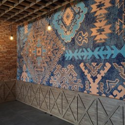 Wall & Poster Profesjonalne tapetowanie - Wzorzysta tapeta w odcieniach błękitu i beżu z motywami etnicznymi, drewniana boazeria z geometrycznym wzorem rombów, ceglana ściana w rogu i sufit z drewnianych belek w restauracji.