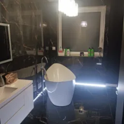 Nowoczesna łazienka z czarnymi marmurowymi płytkami, wolnostojącą białą wanną z podświetleniem LED na podłodze, chromowaną armaturą i designerską lampą sufitową.