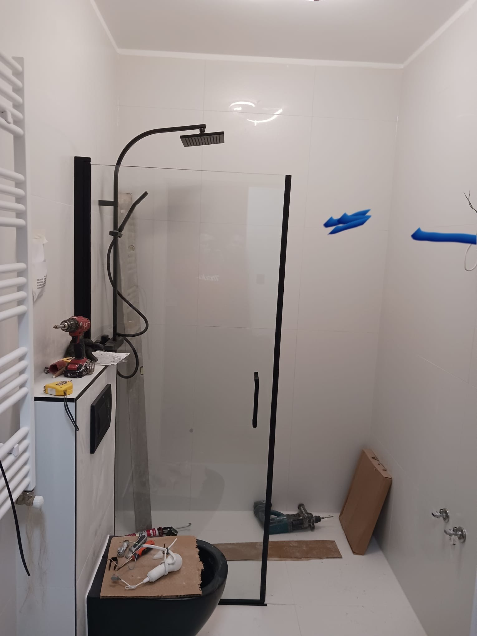 Montaż kabiny prysznicowej typu walk-in z czarnymi profilami, widoczne narzędzia i akcesoria montażowe w łazience z białymi płytkami.