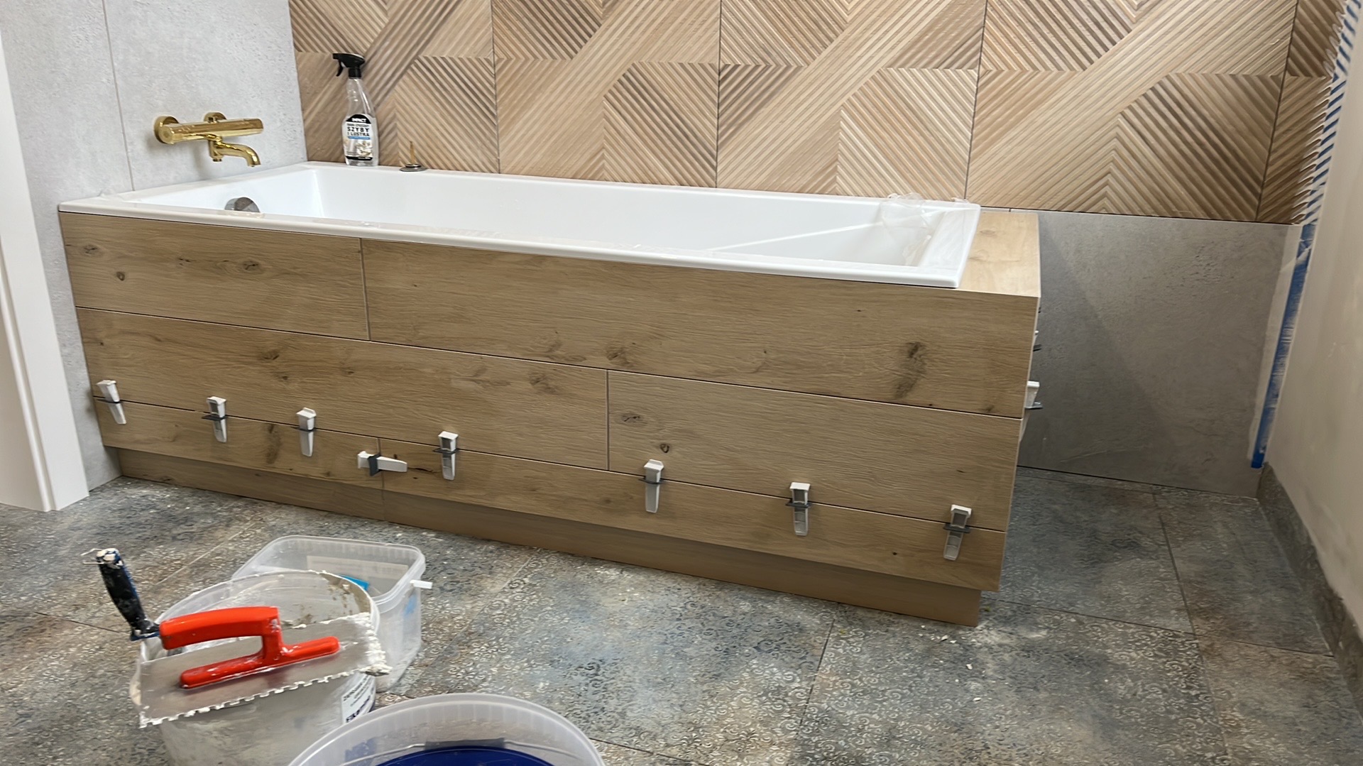 Montaż płytek imitujących drewno na obudowie wanny, widoczne klipsy poziomujące, w tle dekoracyjne płytki ścienne, Żabia Wola.