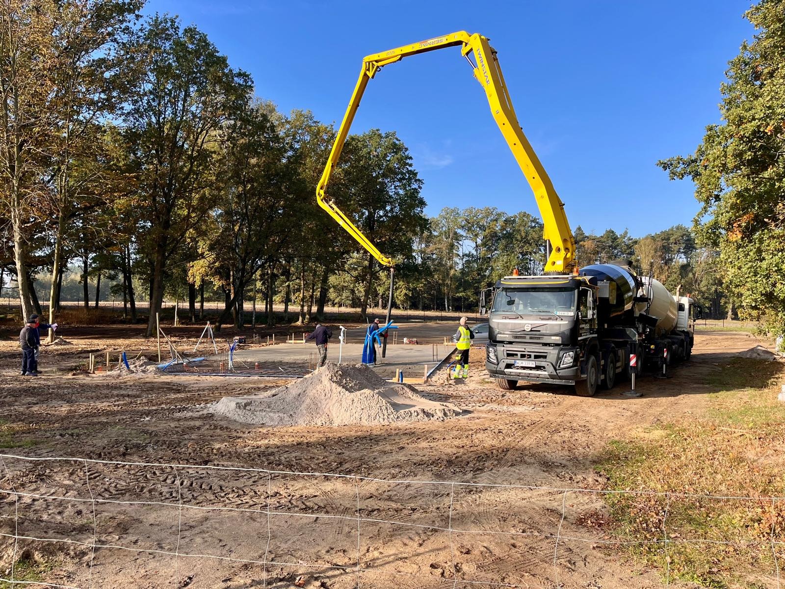 Betonowanie fundamentów domu jednorodzinnego przy użyciu pompy do betonu na tle drzew i błękitnego nieba.